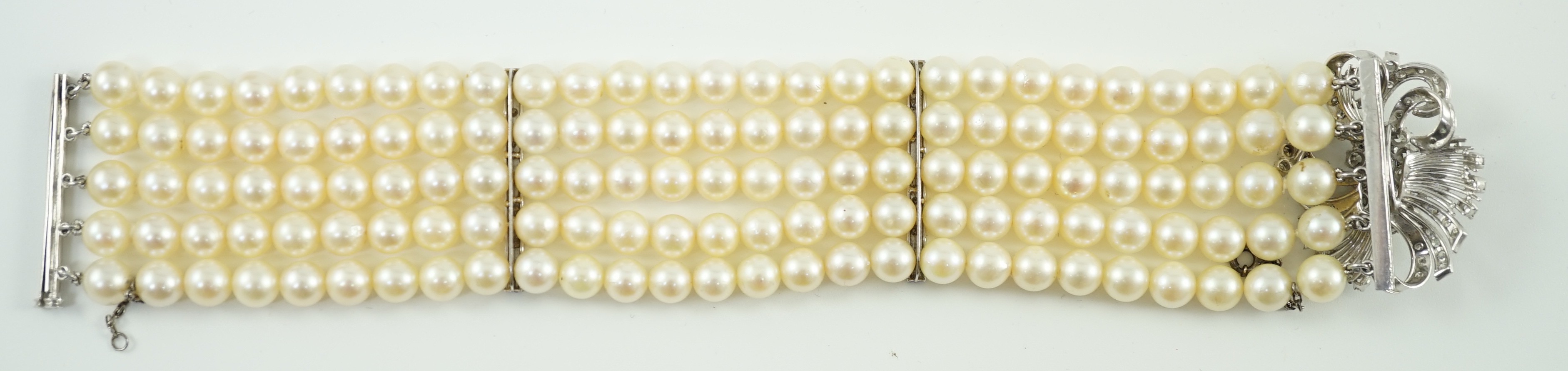 A mid to late 20th century continental quintuple strand cultured pearl bracelet, with white gold and diamond cluster set scroll clasp and diamond set line spacers